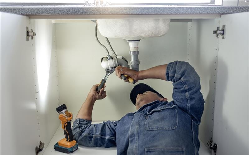 Plumber repairing pipes beneath a bathroom sink in Rocklin